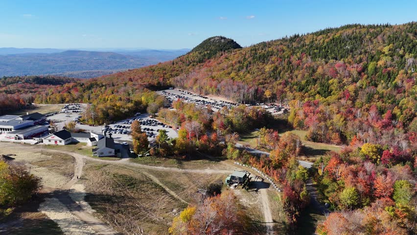 Aerial drone view of White Mountain National Forest in autumn, with vibrant fall foliage, rolling hills and scenic landscape with colorful trees under clear blue sky in New England wilderness