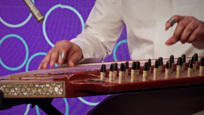 A musician in traditional Saudi attire playing the qanun, a classical
Middle Eastern string instrument. The performer’s hands skillfully pluck the
strings using finger picks.