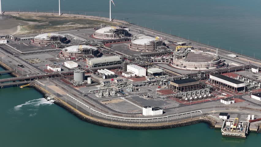 High angle view showing a large liquefied natural gas terminal located on a coastal port, complete with storage tanks, processing facilities, and a maritime jetty for tankers