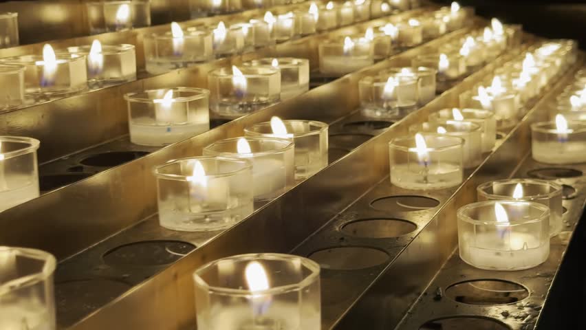 Warm close-up of many lit candles in a dark Italian church or cathedral.