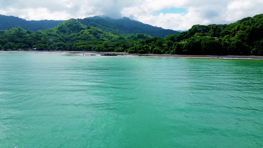Aerial tracking shot of turquoise ocean water meeting a lush green coastline.