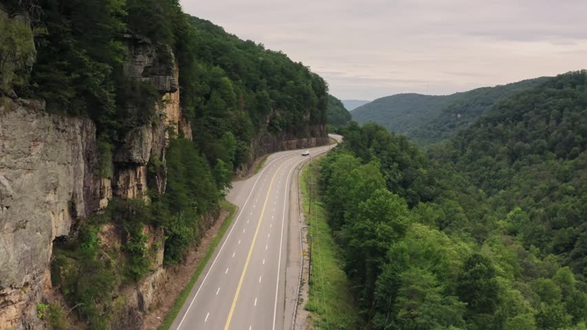 Scenic road passing through green valley surrounded by forest and hills.