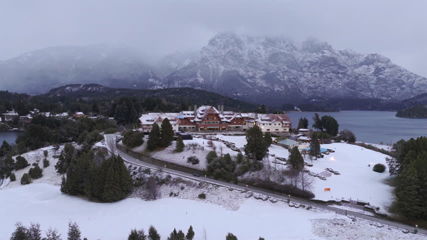 Aerial view of Llao Llao Hotel in Bariloche during snowfall showing luxury resort in Patagonia with mountains lake and winter atmosphere.