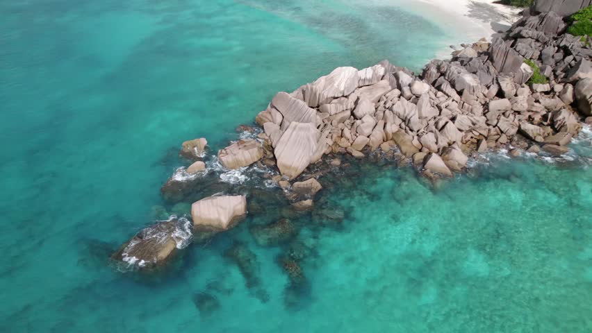 Panning drone of granite stones between grand anse beach and petite anse, along water, La Digue, Seychelles 30fps 006