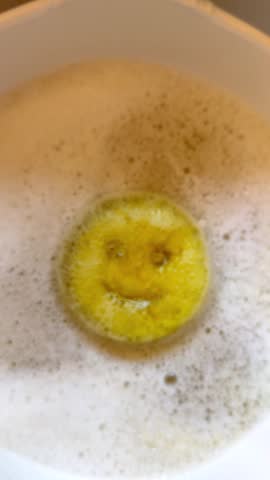 Vertical video - Closeup of a cute, yellow smiling face scouring sponge, floating on top of soap suds in a sink bowl after washing up.