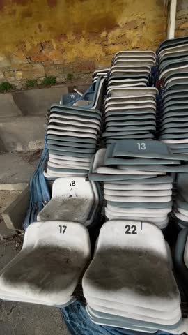 Vertical stock video stacked numbered seats dusty warehouse setting with weathered plastic seating piled against peeling yellow brick wall closeup vertical pan shows numbers and,