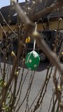 Vertical stock video showing easter egg hanging on budding branch in suburban street, soft sunlight, blurred cars and house roofs, green polka dot egg with ribbon, spring festival - Powered by Shutterstock - Get 15% off with code: PIKWIZARD15