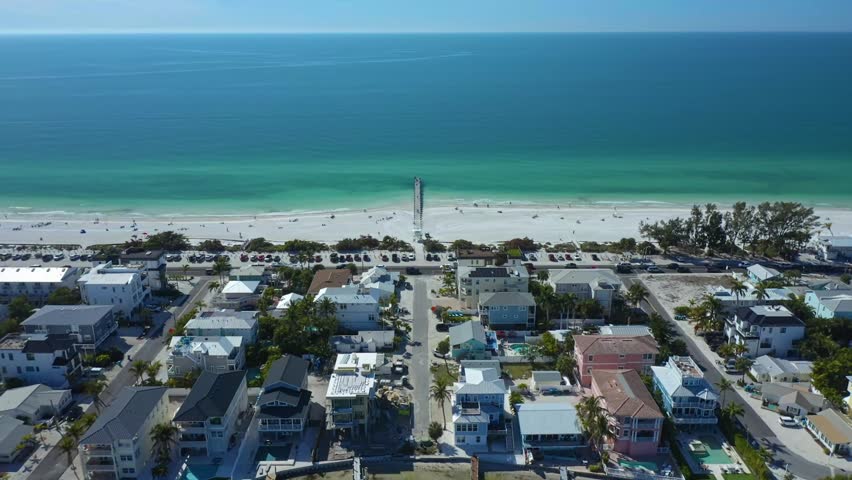 A pier stretches into the quiet sea, flanked by rows of beachfront homes and parked cars. Ideal for real estate or travel content.