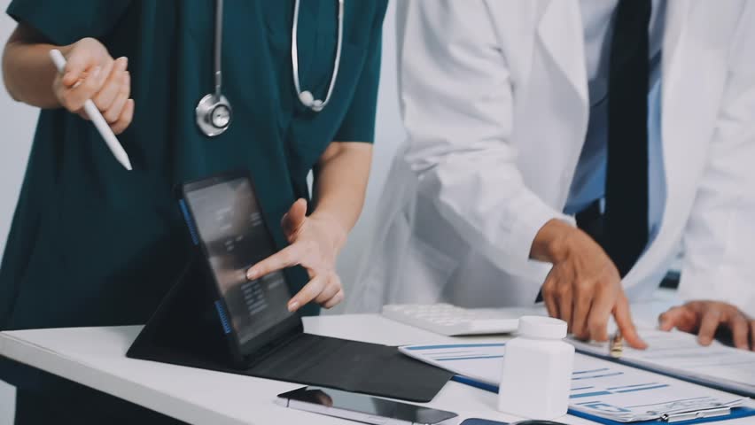 A vibrant red anatomical heart model and a stethoscope on a desk with two doctors having a medical consultation in the background.