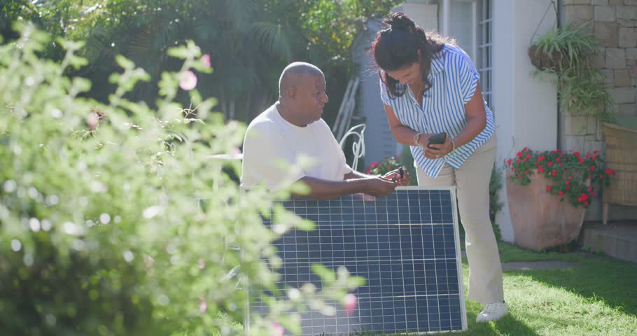 African American couple in yard he showing plug she coming holding phone checking solar panel angle. Photovoltaic, outdoor, lawn, homeowners, connector, renewable, energy
