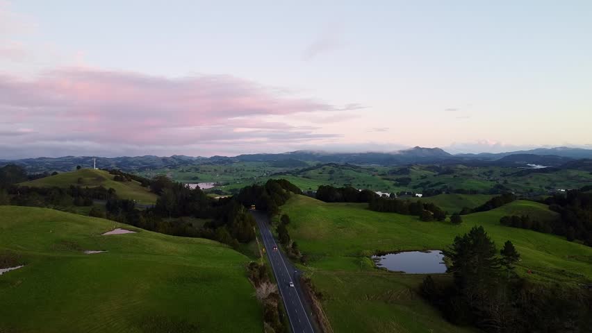 Drone aerial view of road cutting through green countryside landscape in New Zealand.