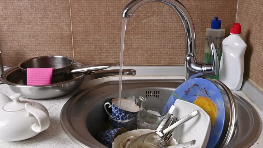 A sink with dirty dishes in a home kitchen. Water flows from the faucet. Concept of routine housework.