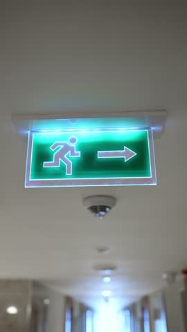 Green emergency exit sign with arrow glowing in the dark. Modern LED fire exit light on ceiling. Concept of safety, evacuation, office security, and public building emergency guidance