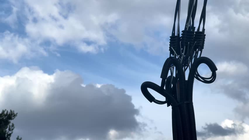 Cables and pipes hang from a pole as clouds gather overhead in the afternoon sky.
