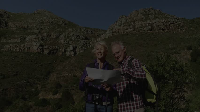 Hiking couple consulting paper map after woman pointing, mist drifting and obscuring ridge. Hikers, mountains, outdoors, trail, backpack, fog, navigation