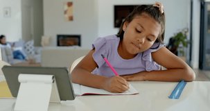 Diverse mom and daughter at counter, daughter writing homework, mom leaning in helping by tablet. Caregiver, child, kitchen, notebook, device, sunlit, modern - Powered by Shutterstock - Get 15% off with code: PIKWIZARD15