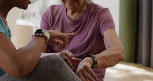 African American caregiver leaning in pointing at smartwatch and tapping phone guiding senior at home. Wearable, tracker, guidance, instruction, interaction, eldercare, engagement - Powered by Shutterstock - Get 15% off with code: PIKWIZARD15
