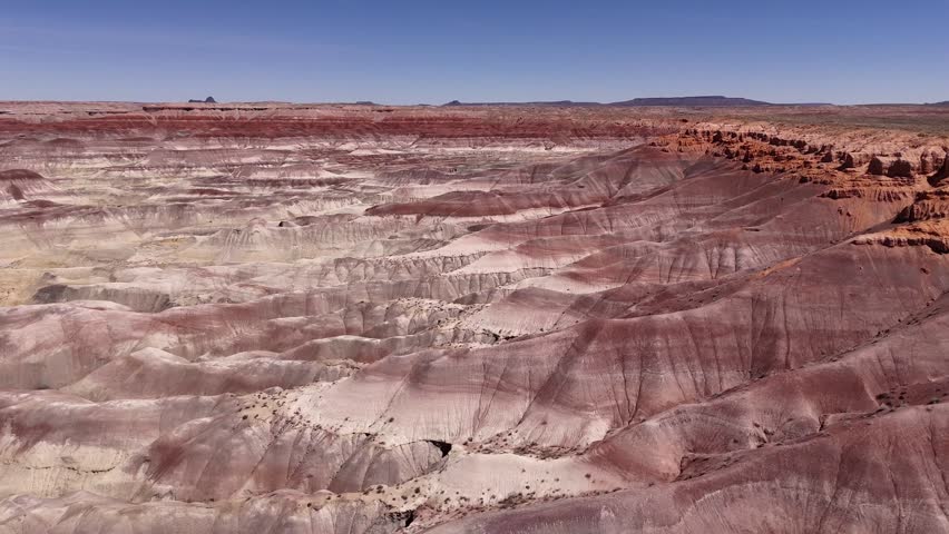 Aerial view of the Little Painted Desert showing colorful layered rock formations and eroded badlands under a clear blue sky in Winslow, Arizona, United States.