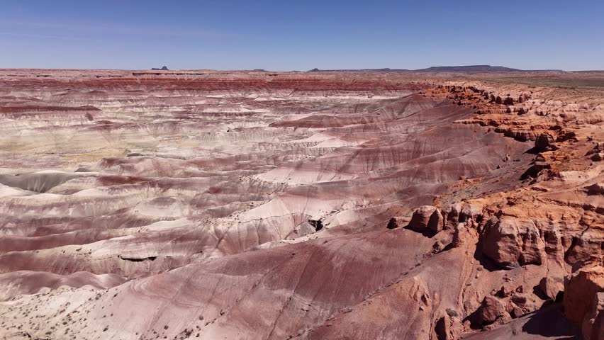 Aerial view of the Little Painted Desert badlands featuring colorful layered rock formations under a clear blue sky in Winslow, Arizona, United States.