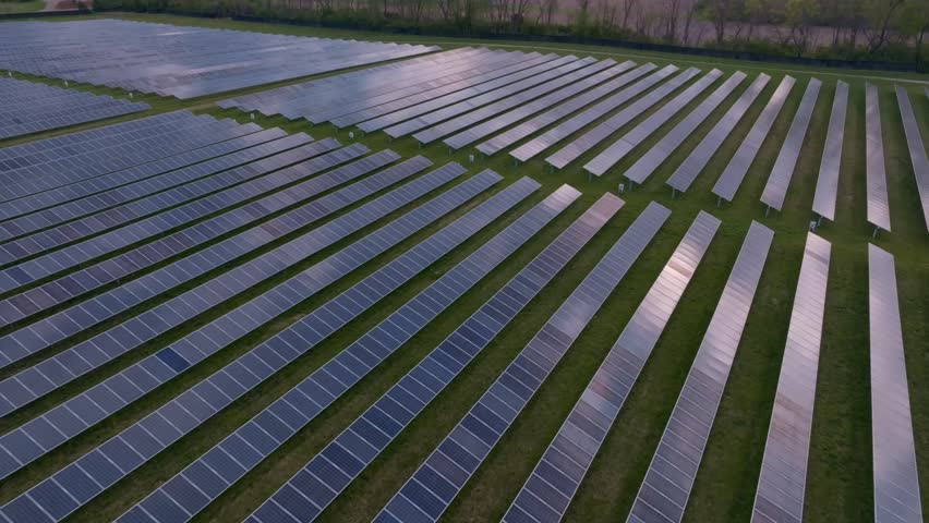 Aerial view of a large solar farm with rows of photovoltaic panels on green grass during sunset in Indianapolis, Indiana, United States.