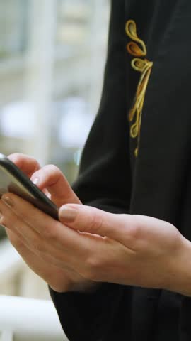 Tapping phone, woman scrolling thumb in mall, causing purple globe over hands, black top, railing. Atrium, smartphone, map, overlay, interaction, skylight, vertical video