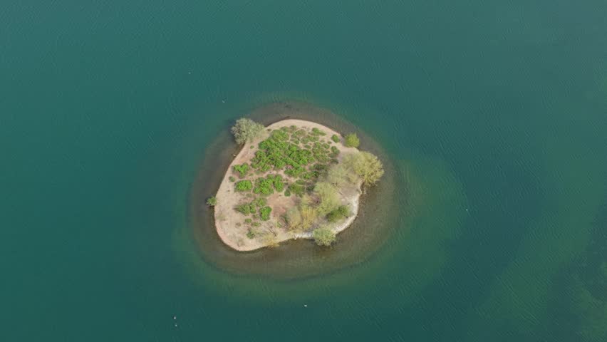 Aerial view of a small island with green vegetation and trees in the middle of Albert Village Lake in Swadlincote, England, United Kingdom.