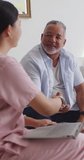Vertical video: Asian nurse in scrubs offering handshake to senior while checking laptop at home. Caregiver, patient, conversation, homecare, livingroom, interior, vertical video - Powered by Shutterstock - Get 15% off with code: PIKWIZARD15