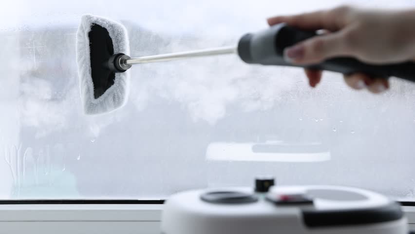 Woman cleaning window with steam cleaner at home, closeup. Camera moving right