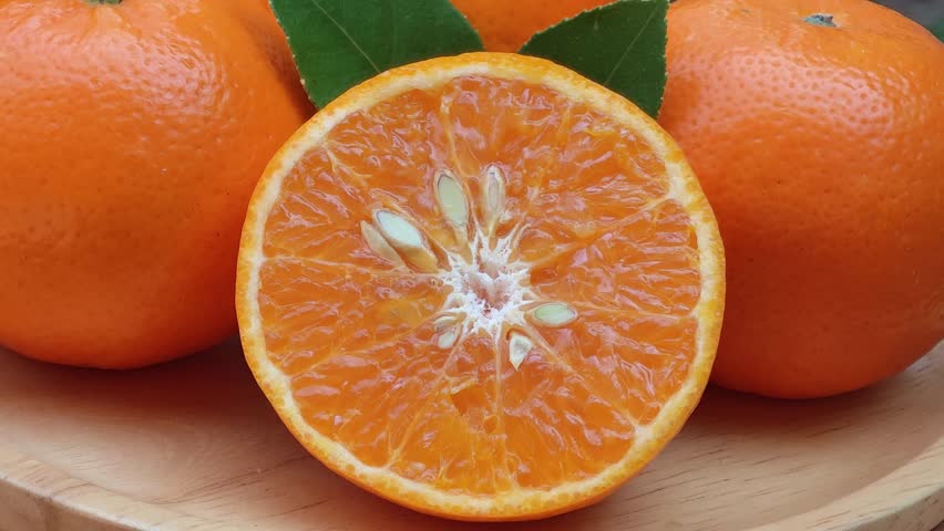 Oranges cut in half with leaves on a wooden tray.