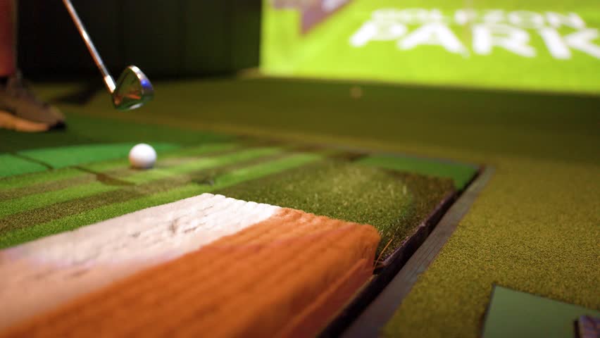 A golfer hits a ball from an artificial turf mat inside a virtual golf simulator
