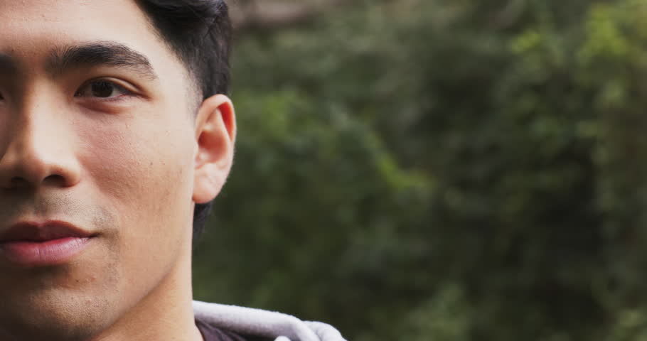 Asian adult man wearing grey hoodie shifting gaze and forming broad smile in forest, copy space. Natural, outdoor, serenity, freshness, emotional, casual, tranquil