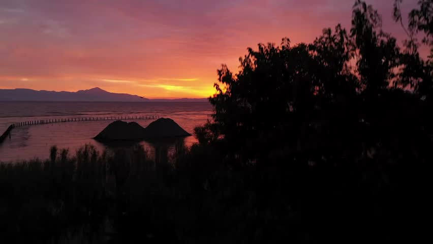 Breathtaking Aerial View of Vibrant Red Sunset Over Calm Lake with Mountain Silhouettes