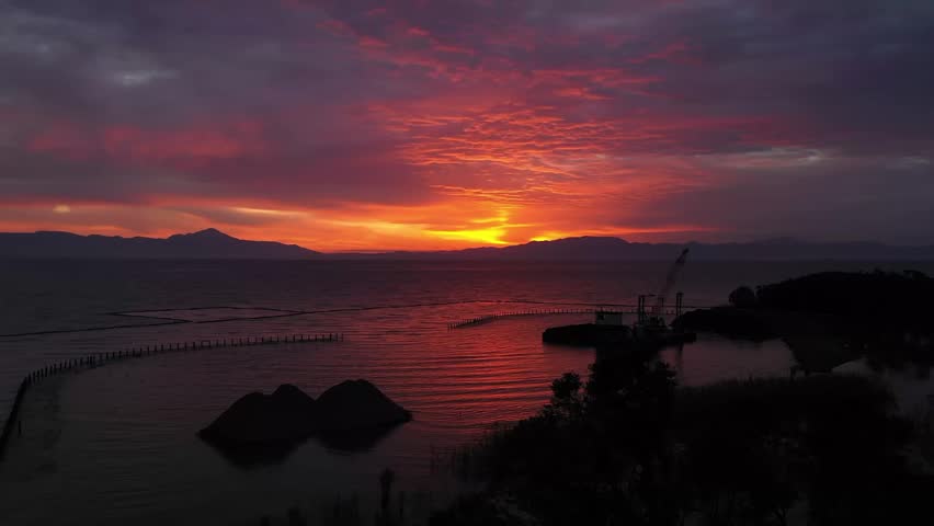 Breathtaking Aerial View of Vibrant Red Sunset Over Calm Lake with Mountain Silhouettes