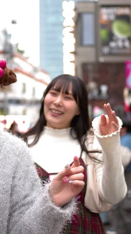 A smiling Japanese woman in a plaid dress talks with friends on a busy street