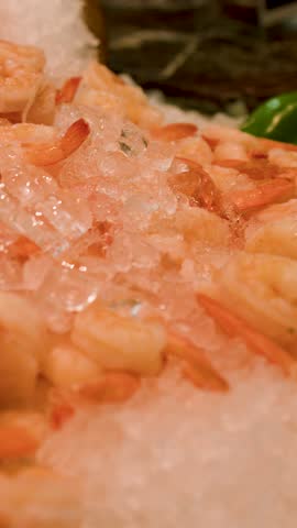 A vertical panning shot reveals chilled shrimp, spotted babylon snails, and mussels on crushed ice