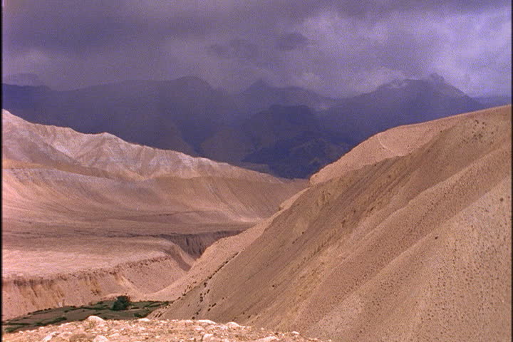 Dry mountains in foreground and dark storm clouds over range looming in background in Mustang, Nepal.