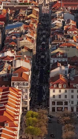 Aerial view of Rua Augusta crowded with people between historic buildings and red-tiled rooftops during golden hour in Lisboa, Lisboa, Portugal.