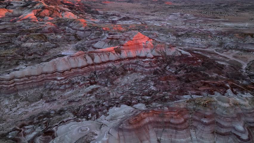 Aerial view of the colorful bentonite hills and rugged badlands terrain glowing under the warm sunset light in Hanksville, Utah, United States.
