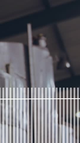Vertical video: Overlay peaking, woman in apron entering, turning to camera and smiling in brewery. Fermentation, tanks, industrial, stainless, pipes, production, vertical video