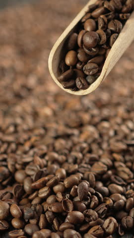 Scooping roasted coffee beans with wooden scoop, close-up.