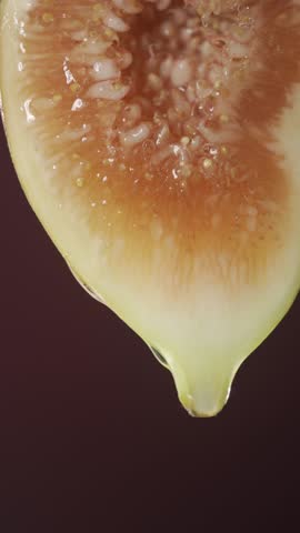Cut in half fig fruit, hanging, with dripping glycerin on a dark maroon background.