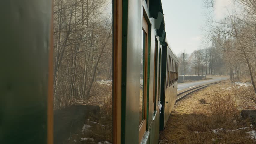Mocanita steam train moves through a winter forest in Romania. Snow covers the ground as the train travels along the tracks surrounded by trees and scenery.