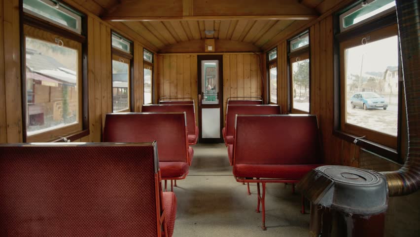 The Mocanita train carriage shows red seats and wooden walls. This train travels through mountains and forests in Romania, offering a glimpse of old transport.