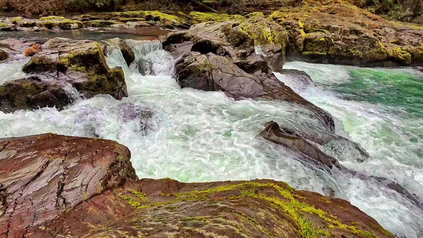 Fast Whitewater Rapids Cascading Over Dark Mossy Rocks in Wild River