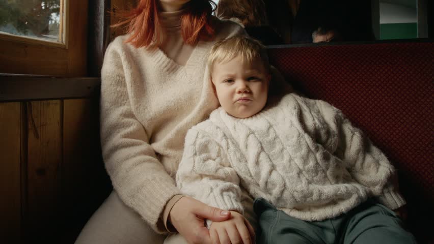 A little boy looks at the camera while sitting in his mother
