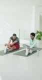 Vertical video: Man and African American woman stretching and folding forward on yoga mats in gym. Fitness, flexibility, companionship, wellness, modern, minimalist, vertical video - Powered by Shutterstock - Get 15% off with code: PIKWIZARD15