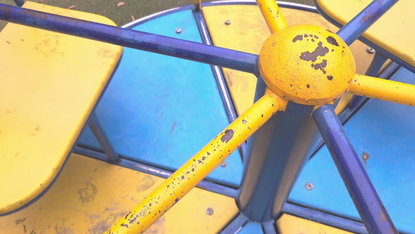 A spinning yellow and blue playground carousel in a public park. Nostalgic childhood, outdoor play, park leisure.