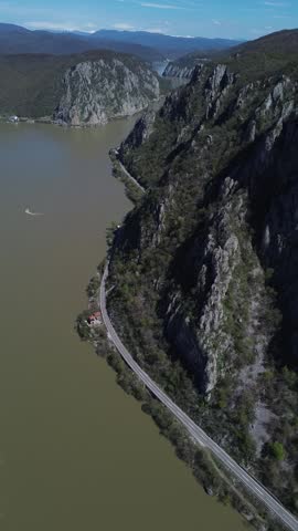 Aerial perspective video of Danube River flowing through narrow Iron Gates section in Djerdap National Park, Serbia. Drone view vertical footage with dramatic limestone cliffs at Kazan gorge during sunny day.