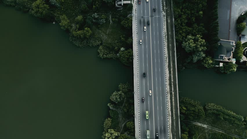 Aerial view of bridge over water with vehicles moving and trees lining, aerial flying drone high view