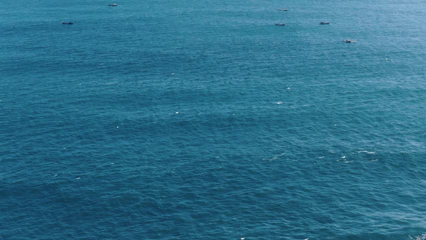 Aerial view of small fishing boats scattered across the deep blue waters of Mesra Beach, Kecamatan Tanjungsari, Daerah Istimewa Yogya, Indonesia.